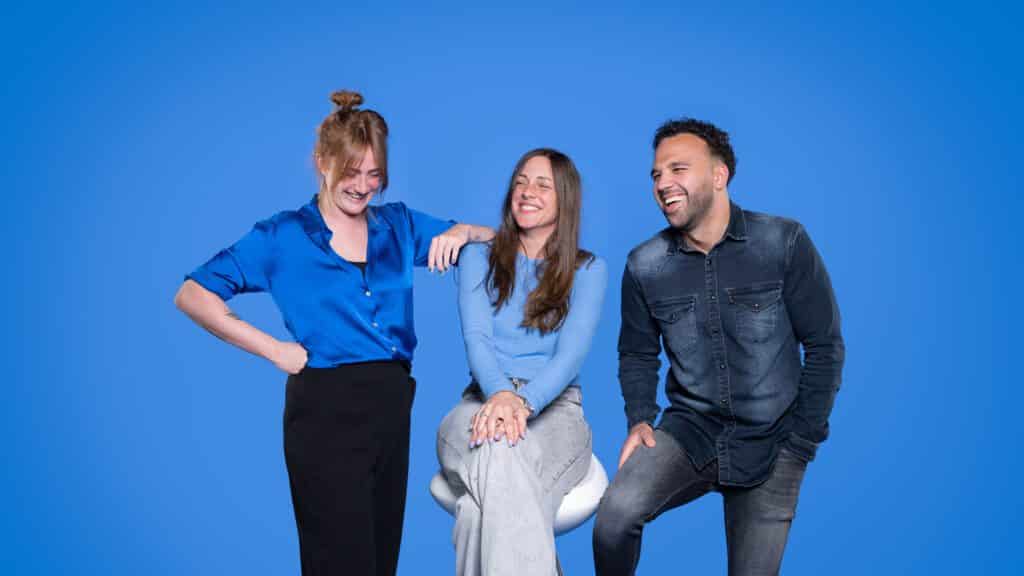 Teamfoto van drie collega’s lachend voor een helderblauwe achtergrond
