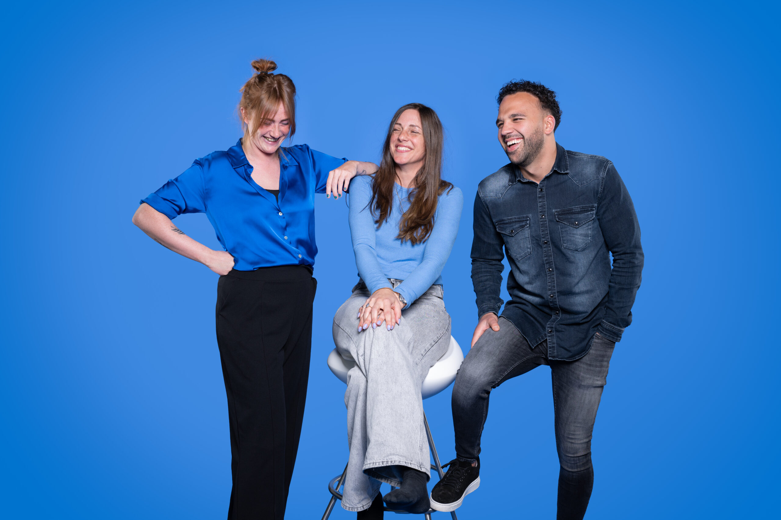 Teamfoto van drie collega’s lachend voor een helderblauwe achtergrond